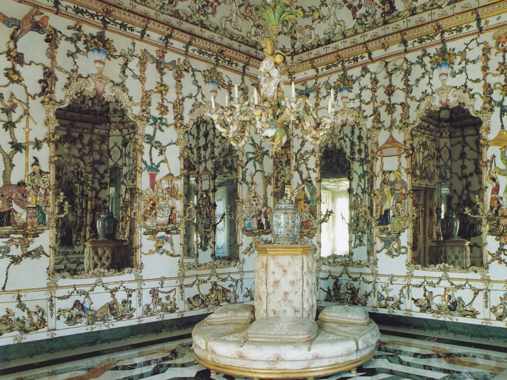 The Porcelain Cabinet at the Royal Palace of Aranjuez, an extraordinary Rococo interior whose walls and ceiling are entirely lined with brightly glazed porcelain panels, mirrors and sculptural chinoiserie decoration.